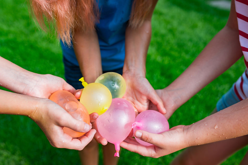 Children hold colorful water balloons together on a sunny green lawn, ready for a playful outdoor game.