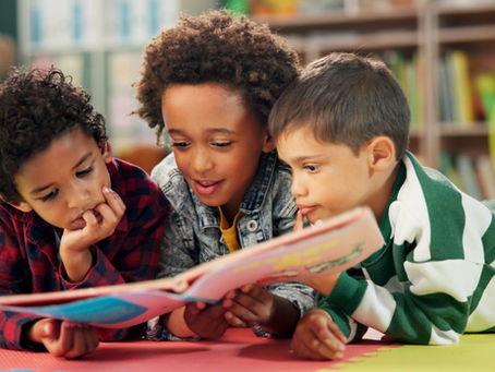 Three young children lay reading a book.