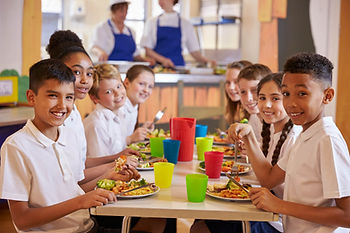 Smiling children in school uniforms sit at a table eating nutritious meals