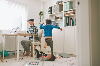 Dad works at a desk while two children play on the floor next to him