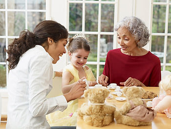 A child, parent, and grandparent sit at a table together having a tea party